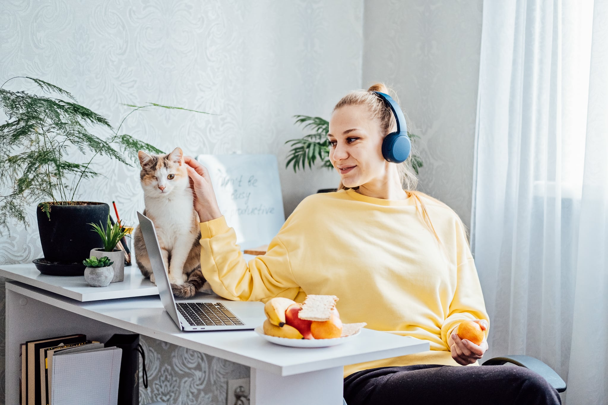 Mental health and work. Work life balance. Young woman in headphones near laptop at home office resting after work. freelancer woman play with cat and eating health food, Taking break time